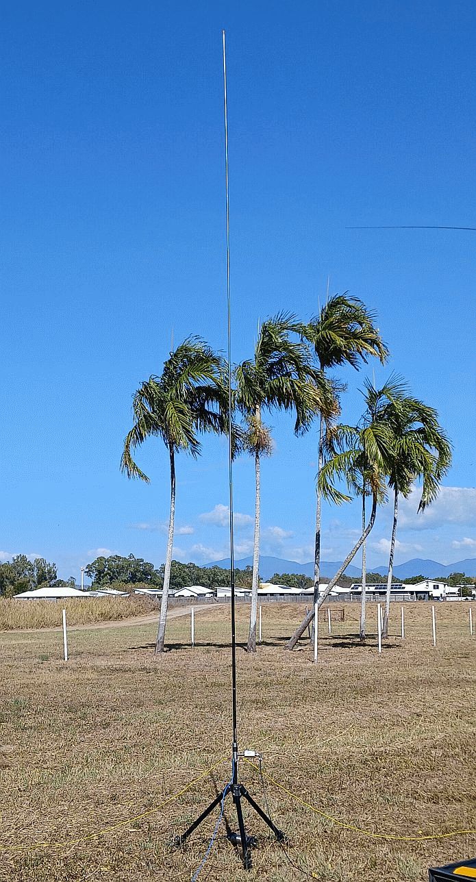 Tall HF vertical antenna against a blue sky with palm trees