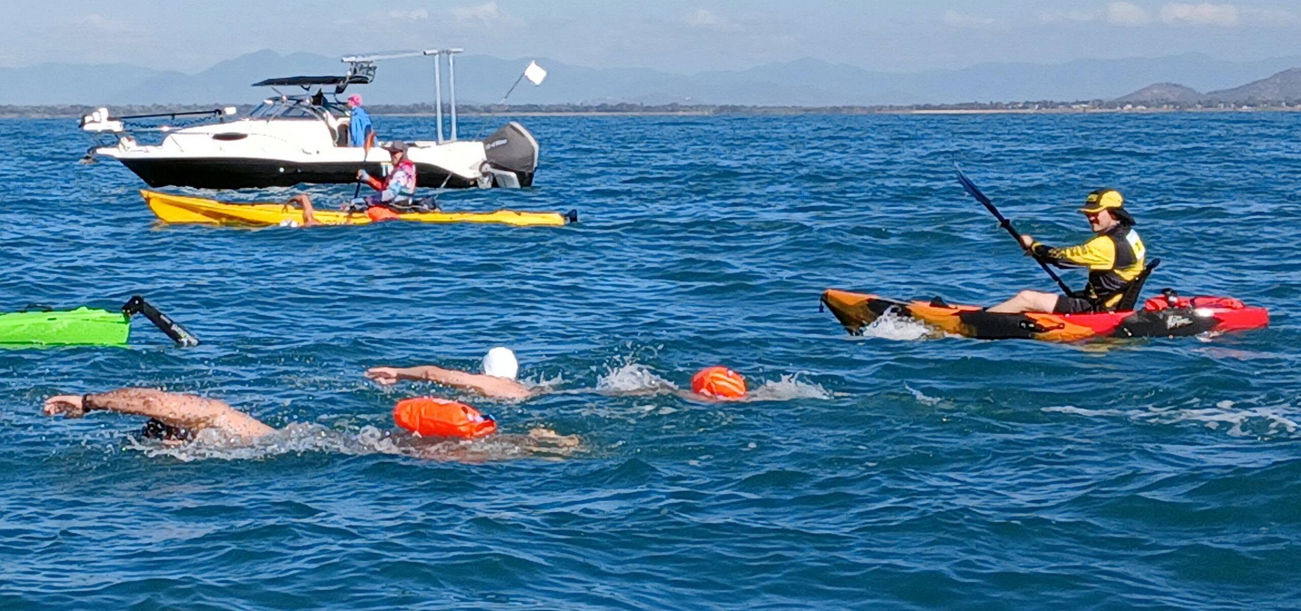 Swimmers crossing the bay with a kayak escort and support boat alongside