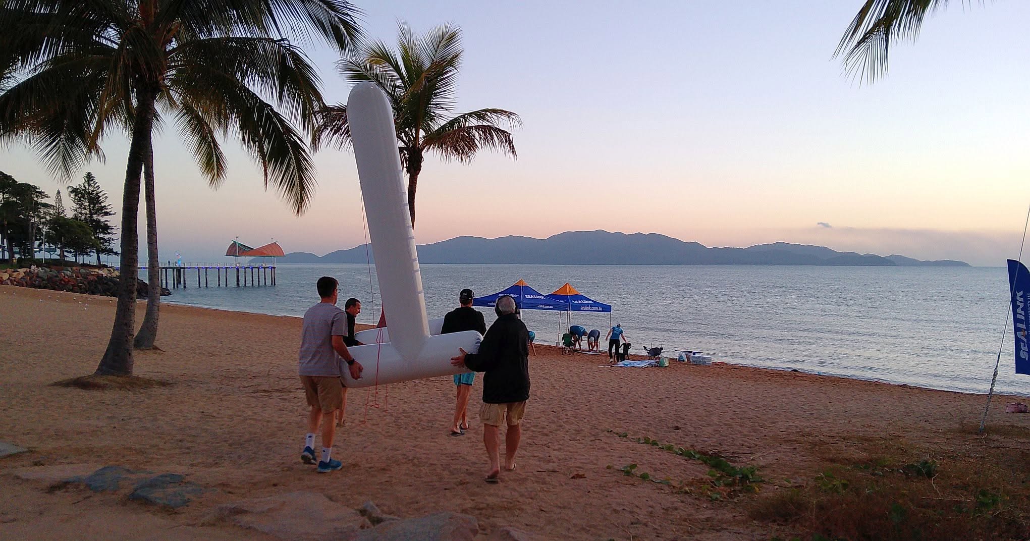 Carrying the inflatable finish arch onto the beach at dawn, Magnetic Island beyond