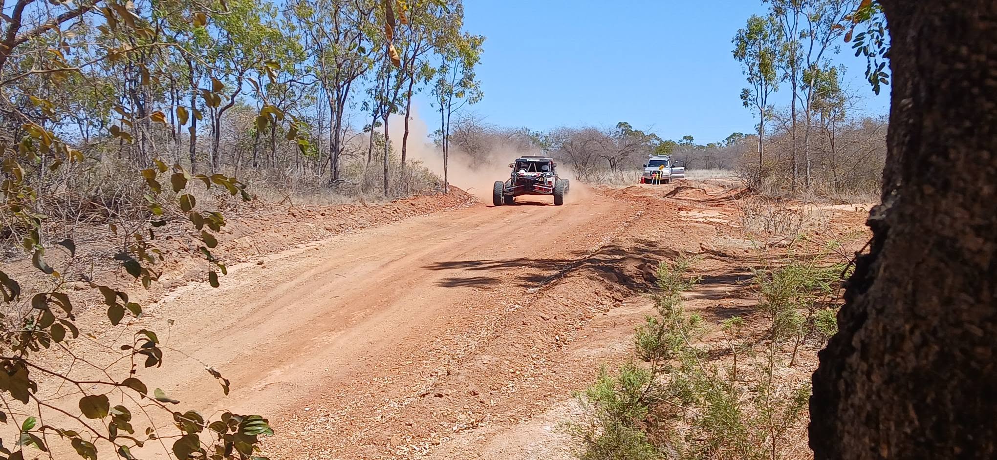 Race buggy approaching along the red dirt track with a recovery vehicle behind